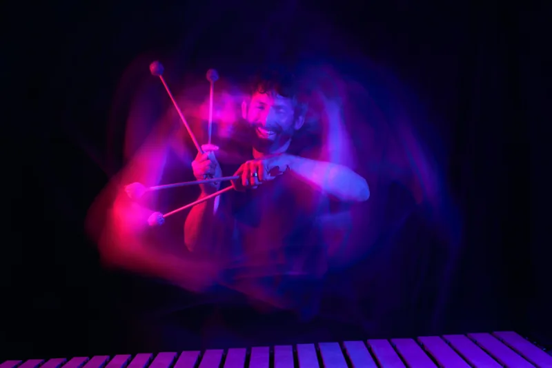 Vibraphonist Chris Dingman playing, mallets in motion, in pink and violet light