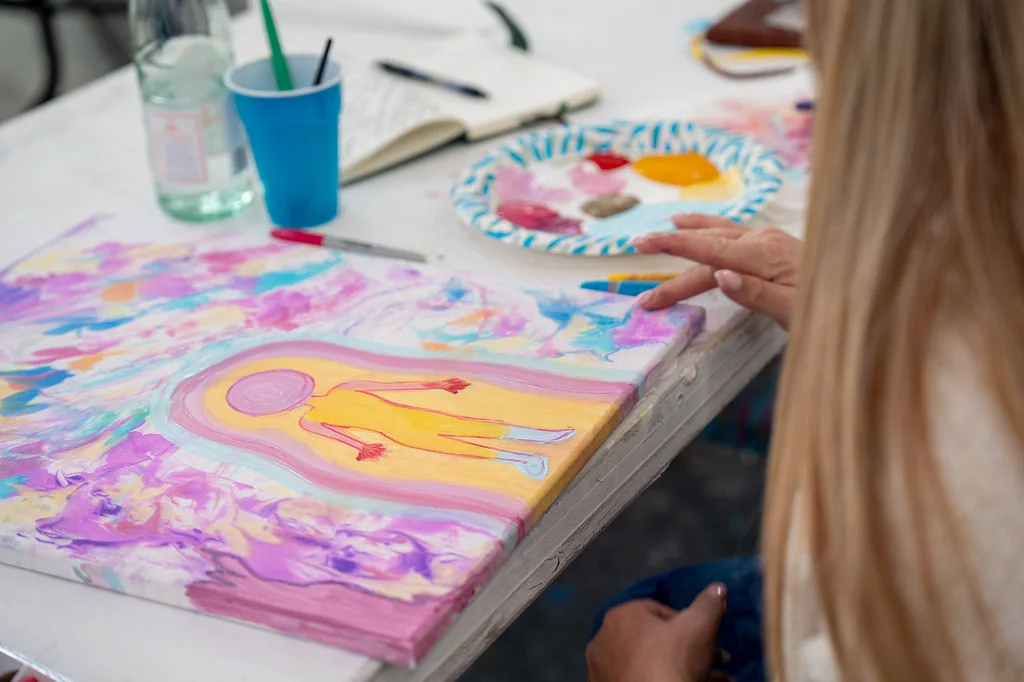 A participant’s hands painting a glowing figure in pastel colors