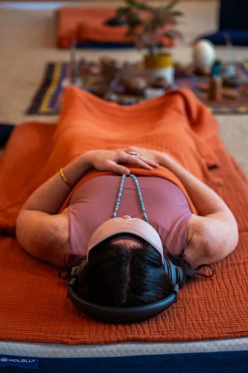 Sarah lying on an orange blanket mid-journey, headphones on, hands resting on her belly