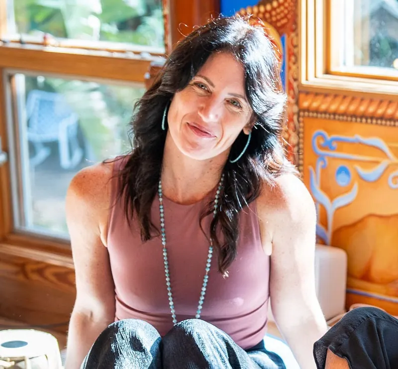 Sarah Burnett seated in her warm, colorful healing space